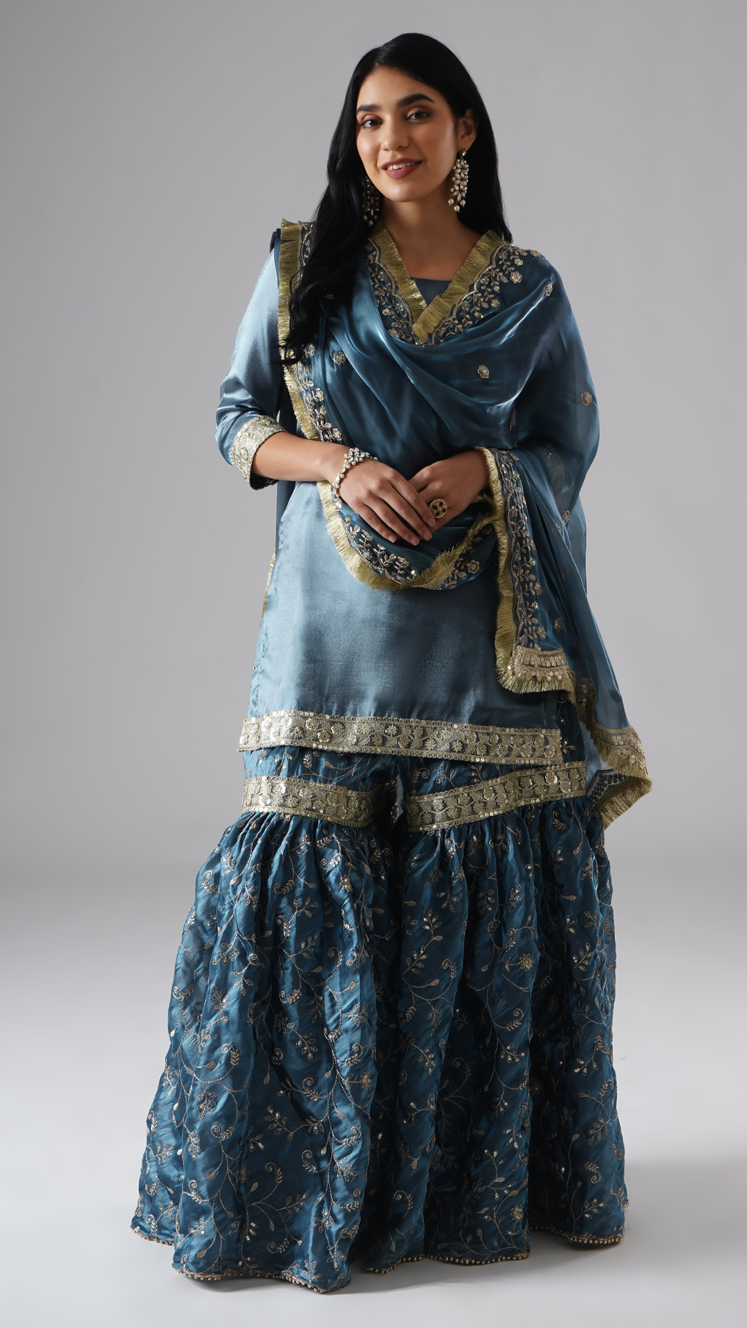 Front view of model wearing Zahrat’s Tehzeeb-e-Aab teal blue gharara set, styled with draped dupatta, showcasing the complete ensemble.