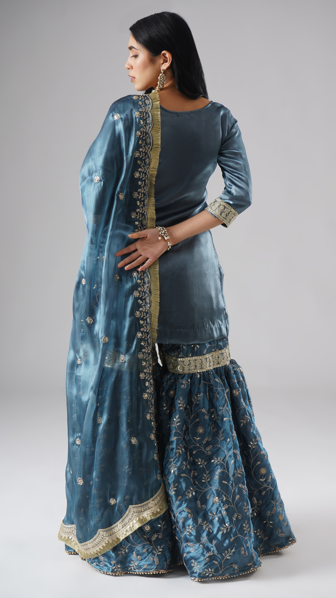 Model styled in the Tehzeeb-e-Aab teal blue gharara set by Zahrat, back view highlighting the full outfit and dupatta drape.