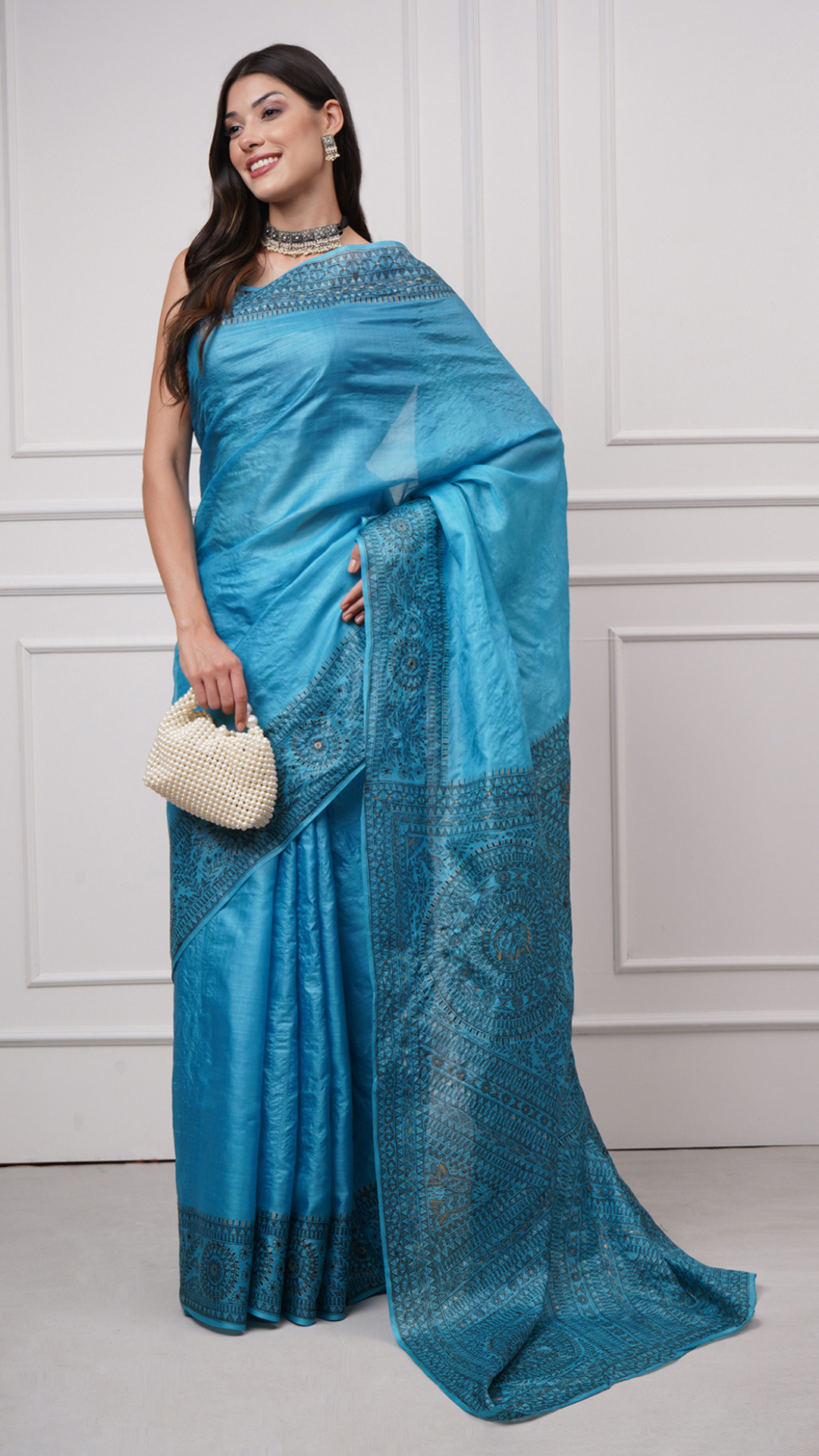 Styled shot of model wearing Neelambara – Azure Madhubani Silk Saree by Zahrat, paired with a pearl handbag, reflecting a refined blend of tradition and modern elegance.