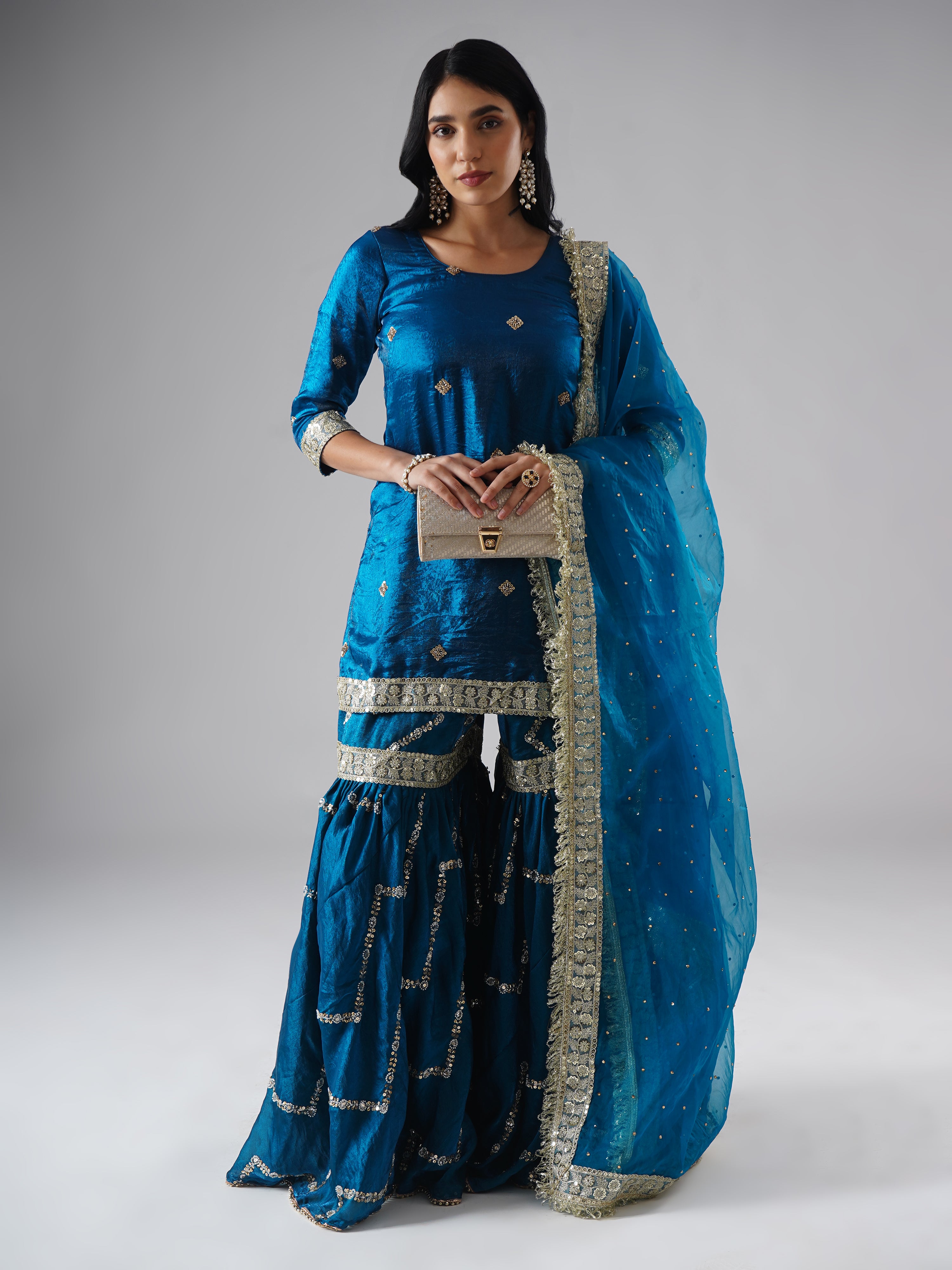 Full outfit of the Neelafshan – The Teal Sapphire gharara set by Zahrat, styled with a clutch, highlighting the gharara, kurta, dupatta, and accessory.