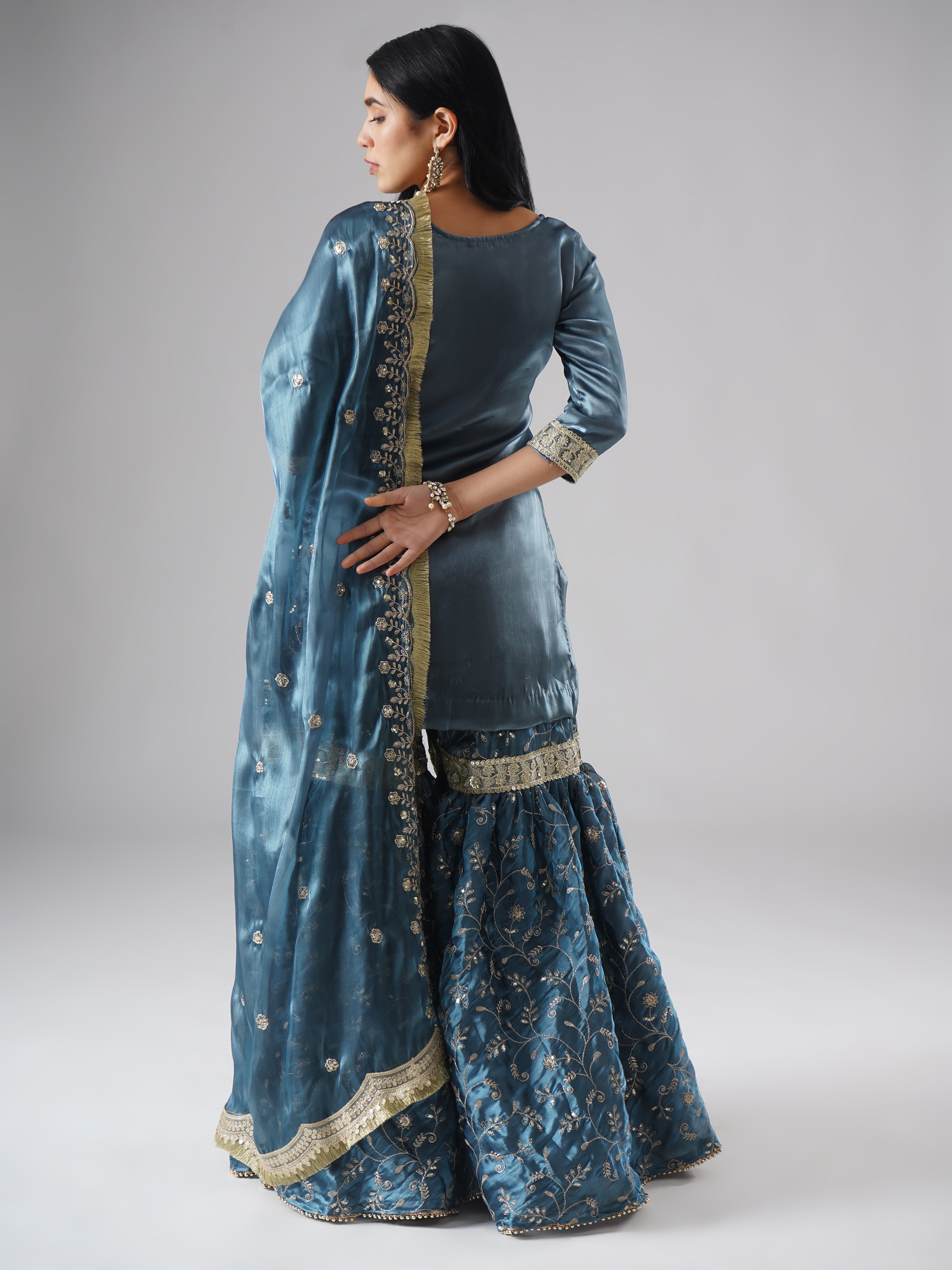 Model styled in the Tehzeeb-e-Aab teal blue gharara set by Zahrat, back view highlighting the full outfit and dupatta drape.