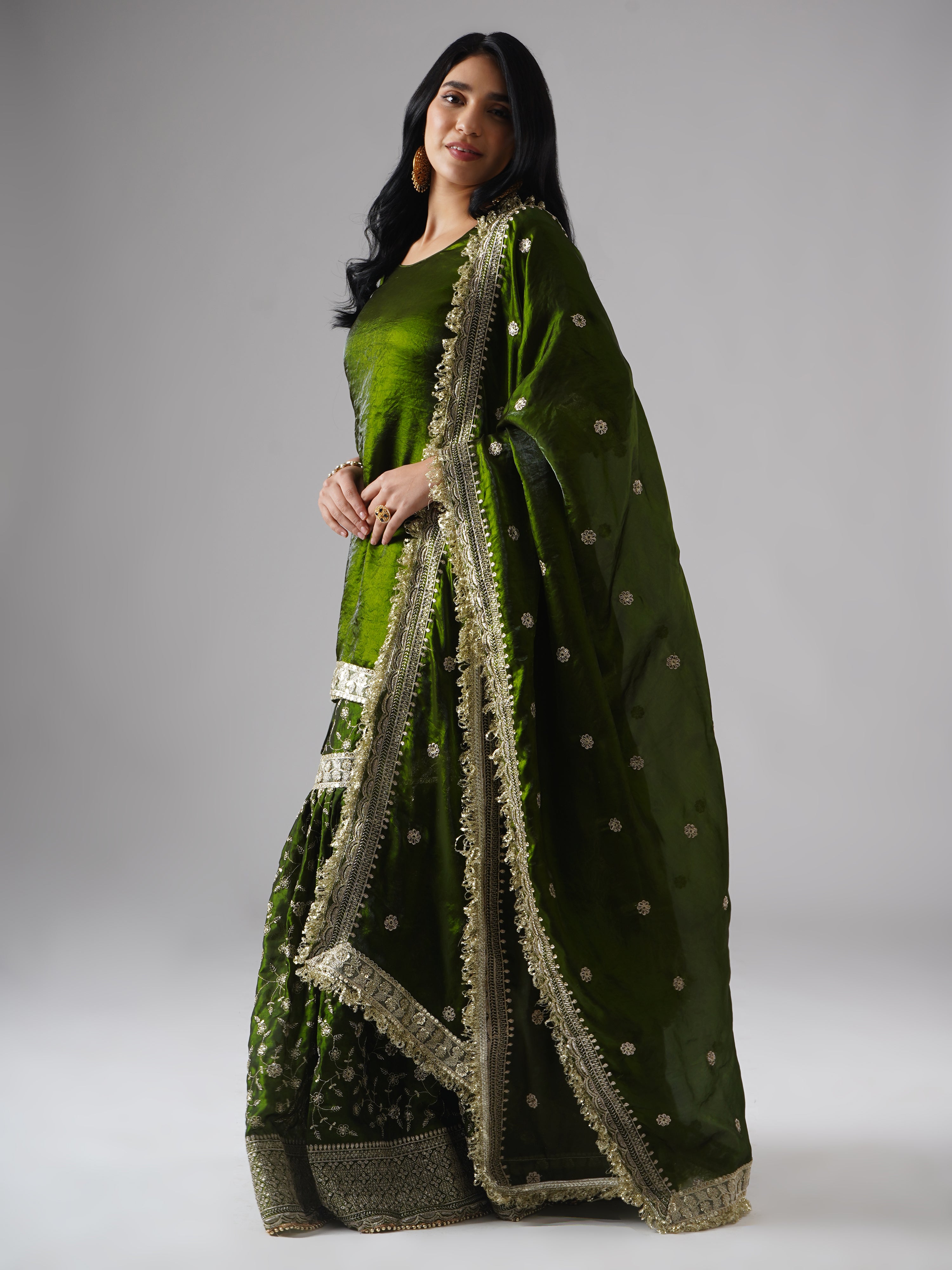 Model styled in the Khushrang Henna Gharara by Zahrat, left side view highlighting the flowing dupatta and full outfit in jewel-toned henna green.