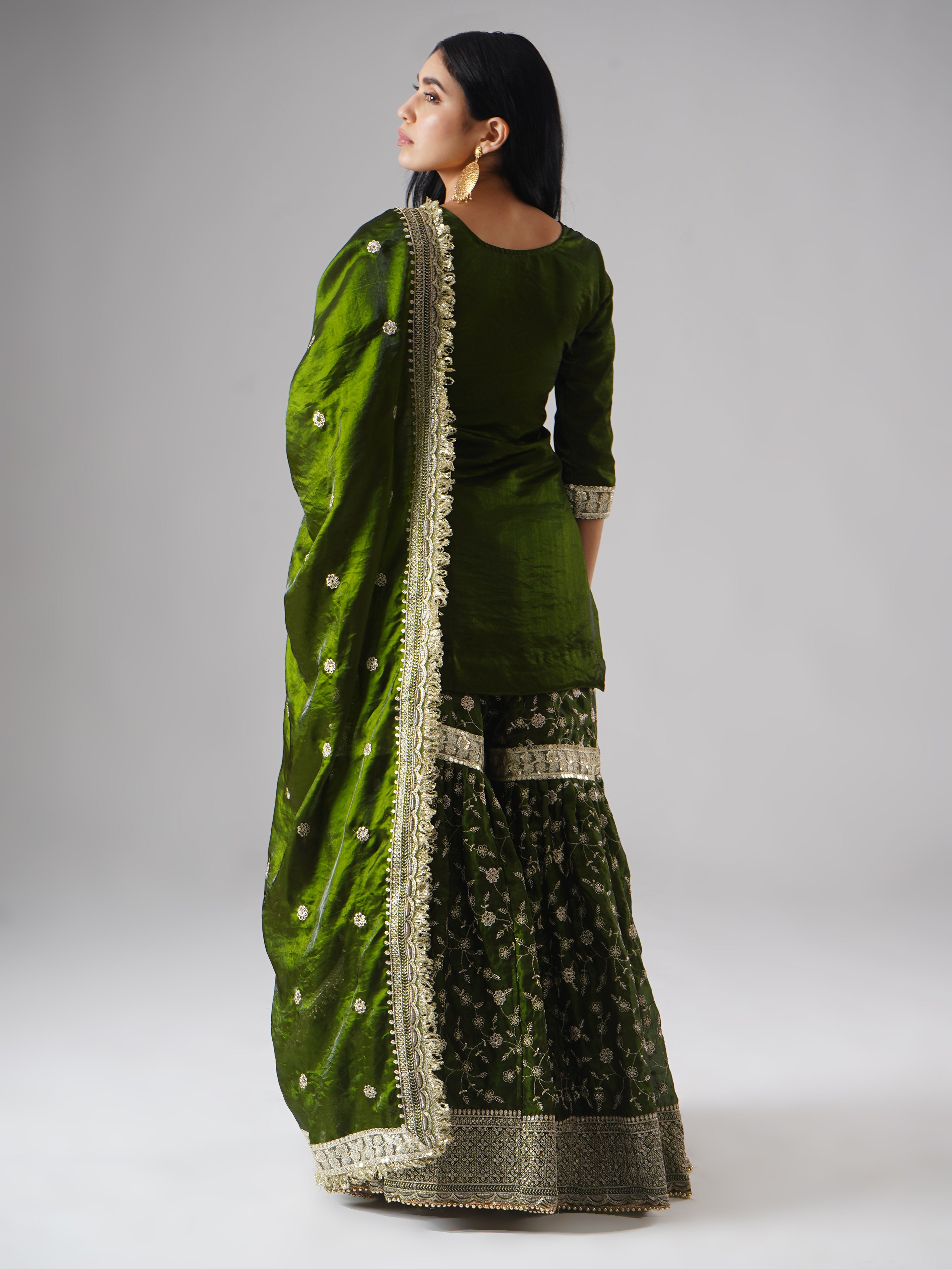 Backside view of model wearing Zahrat’s Khushrang Henna jewel-toned henna green gharara set with dupatta draped gracefully.