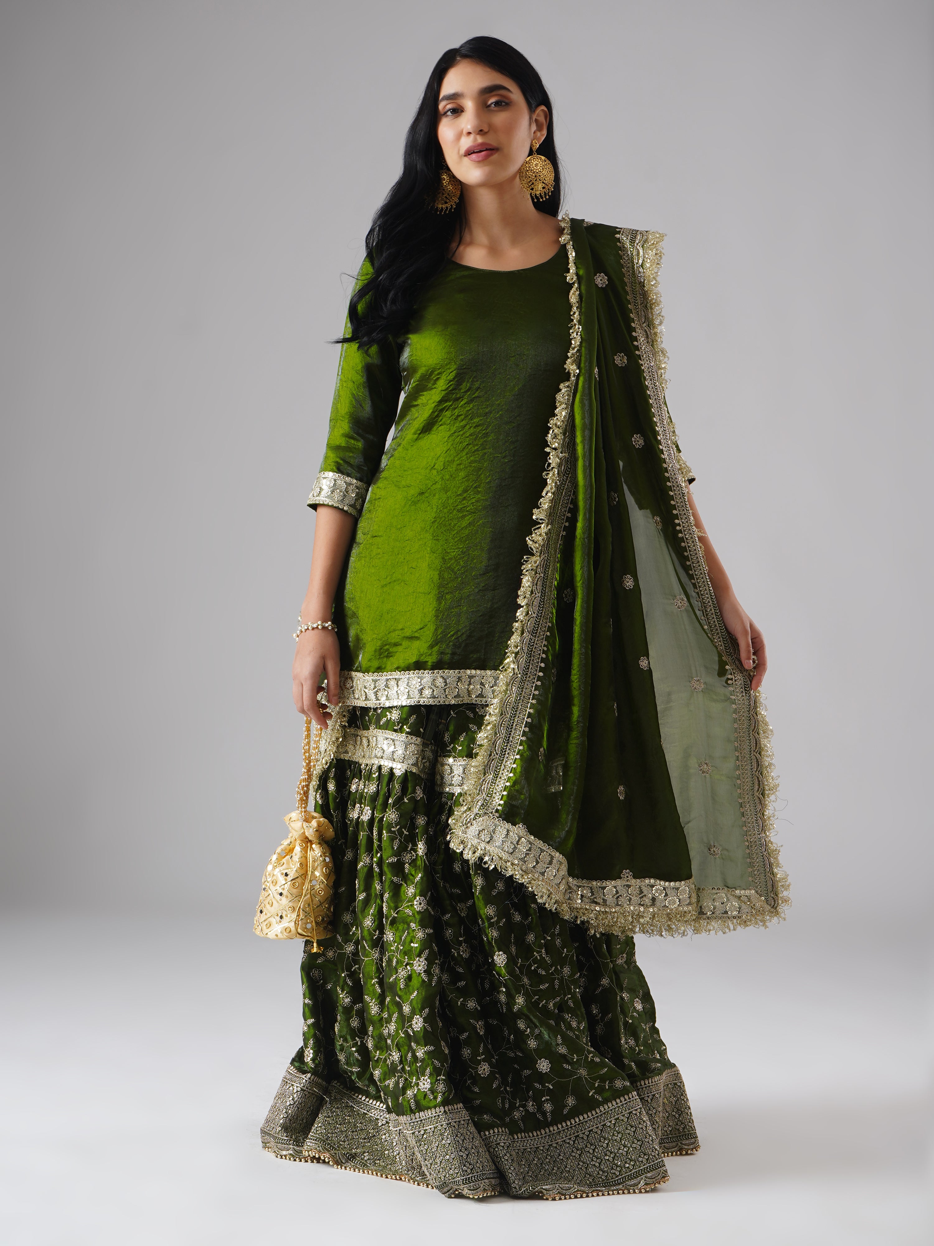 Front view of model wearing Zahrat’s Khushrang Henna jewel-toned henna green gharara set, styled with a potli bag and showcasing the complete ensemble.