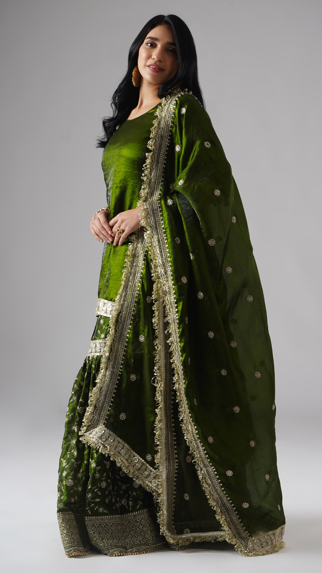 Model styled in the Khushrang Henna Gharara by Zahrat, left side view highlighting the flowing dupatta and full outfit in jewel-toned henna green.