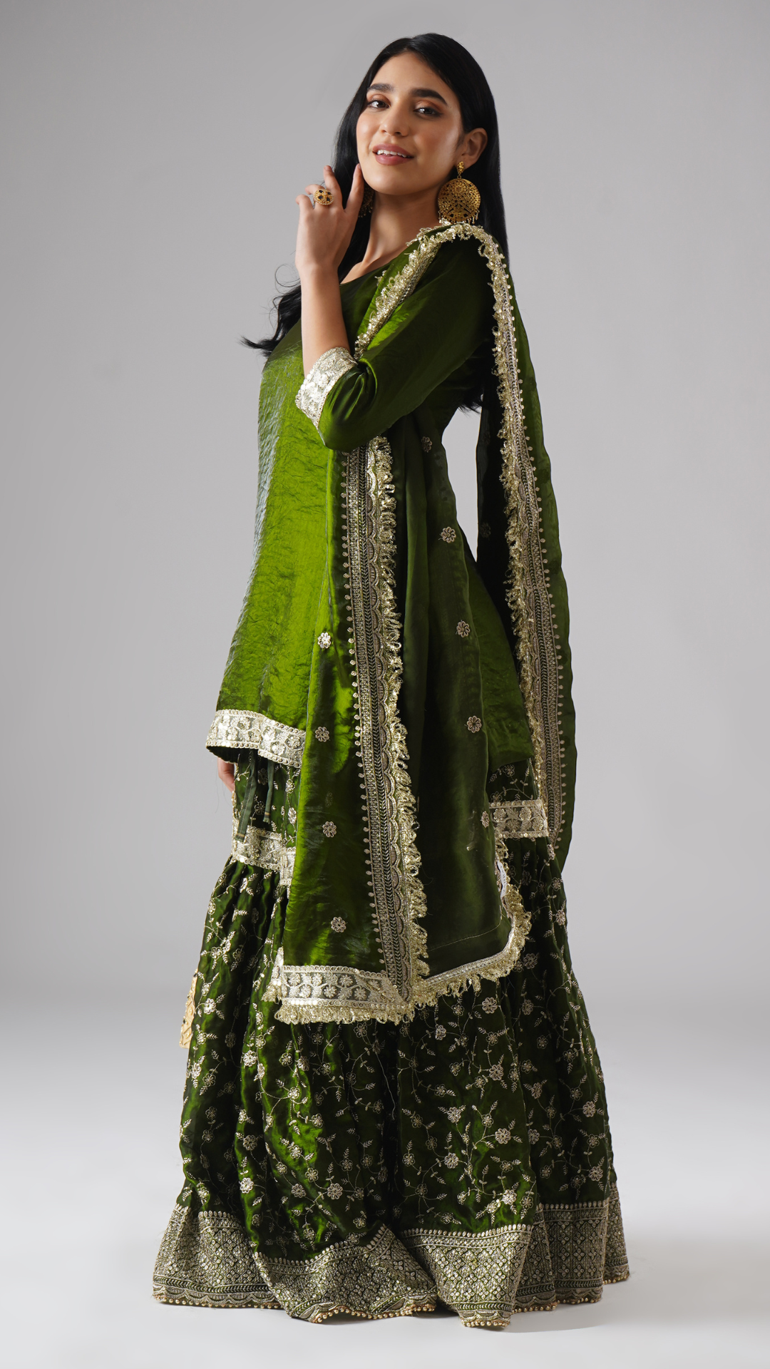 Model styled in the Khushrang Henna Gharara by Zahrat, side view highlighting a festive dupatta drape and the full outfit in henna green.