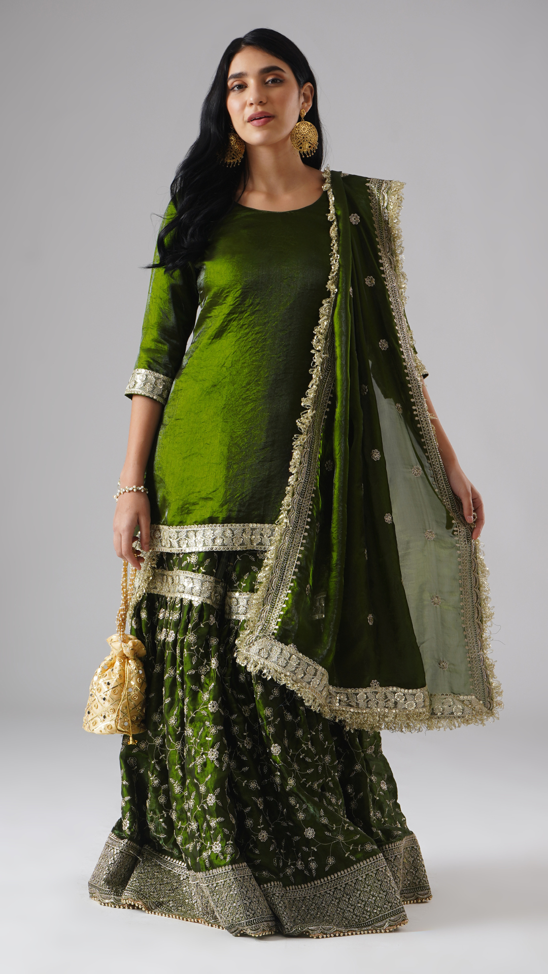 Front view of model wearing Zahrat’s Khushrang Henna jewel-toned henna green gharara set, styled with a potli bag and showcasing the complete ensemble.