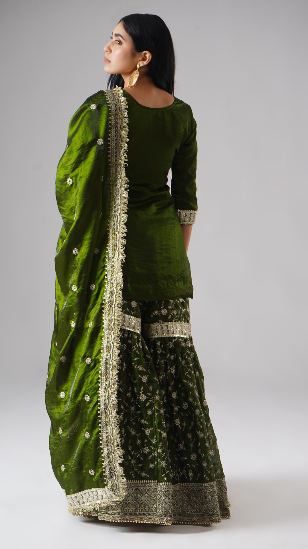 Backside view of model wearing Zahrat’s Khushrang Henna jewel-toned henna green gharara set with dupatta draped gracefully.
