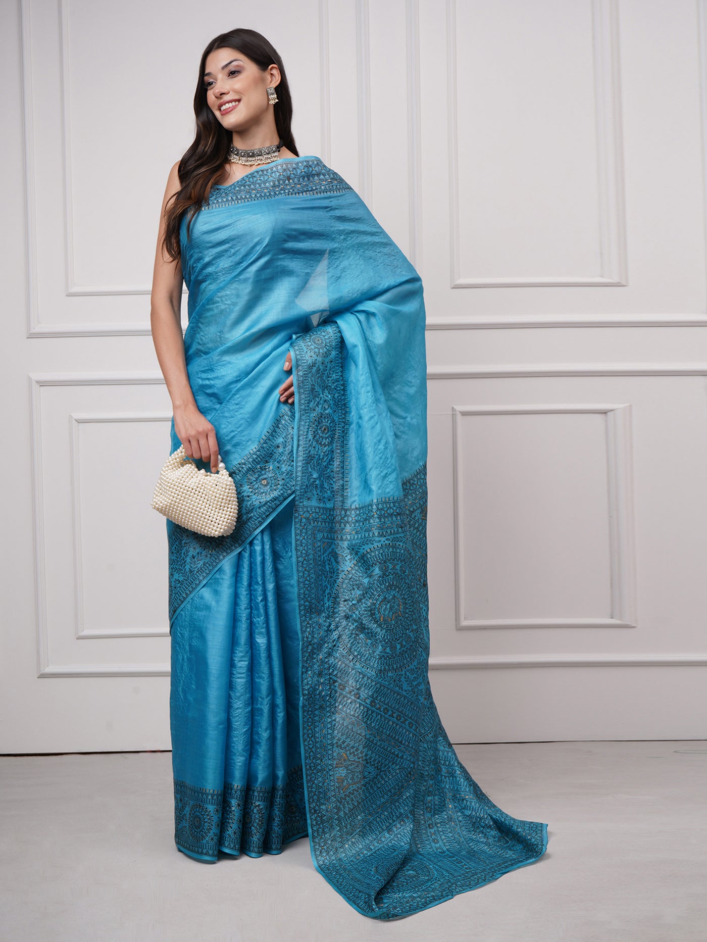 Styled shot of model wearing Neelambara – Azure Madhubani Silk Saree by Zahrat, paired with a pearl handbag, reflecting a refined blend of tradition and modern elegance.