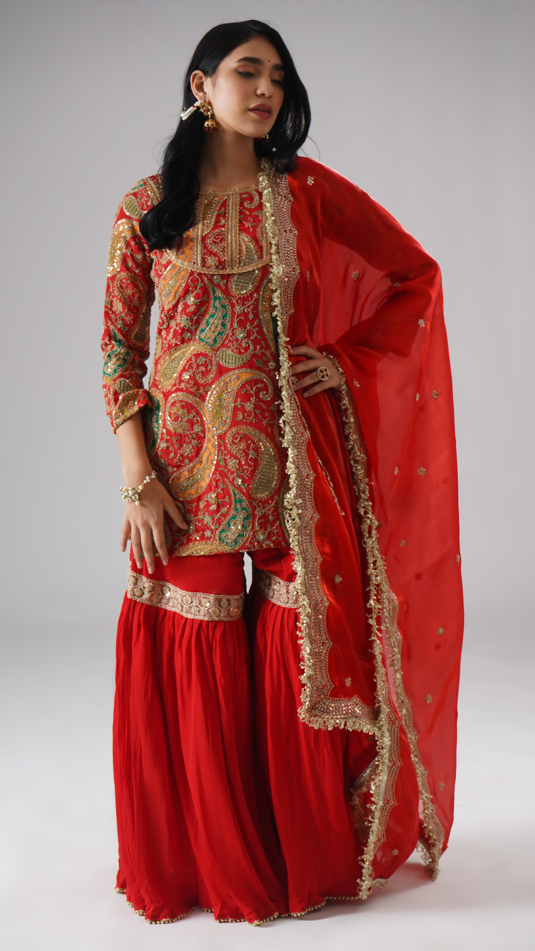 Front view of model wearing Zahrat’s Mehroza crimson red gharara set, showcasing the dupatta draped fully from the side and the complete ensemble.