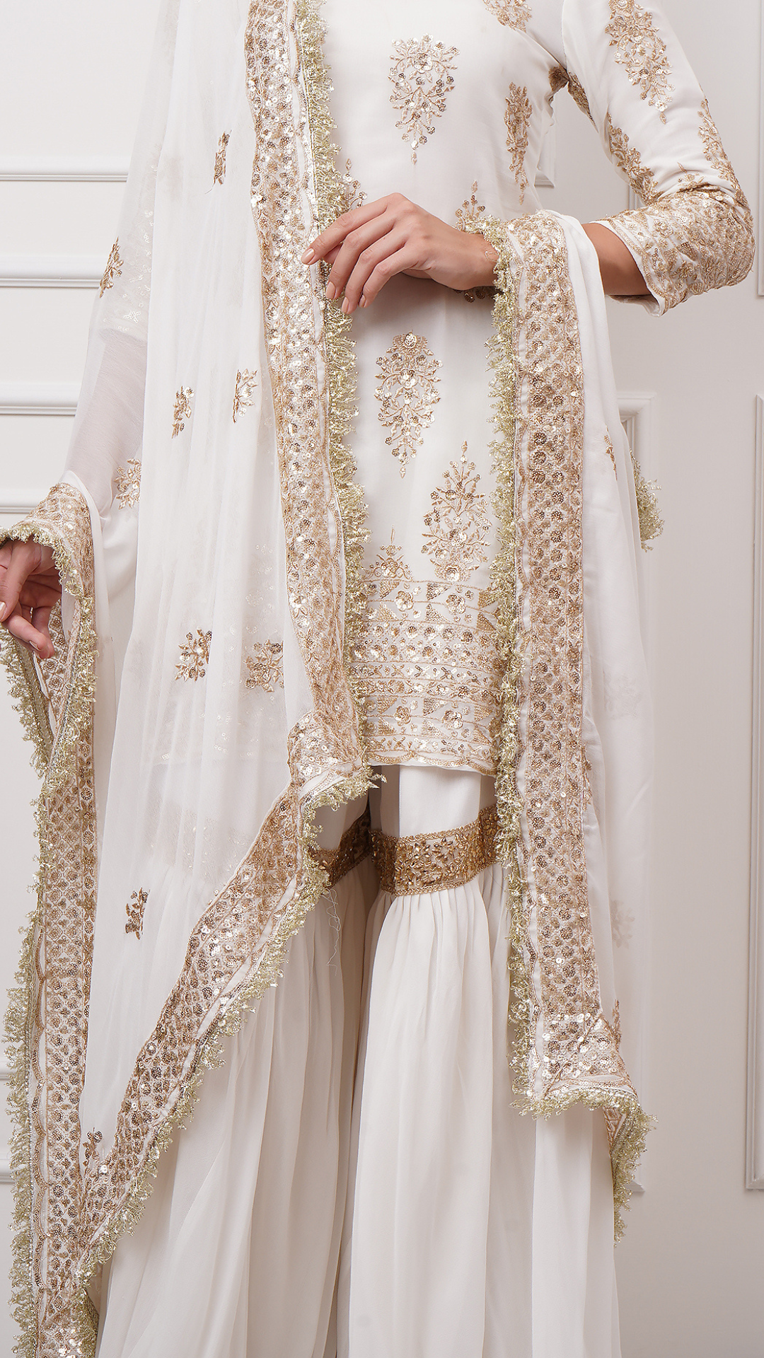 A close-up shot of Naura – White Embroidered Gharara Set by Zahrat showcasing the gold embroidered kurta, dupatta and a plain white flared harara.