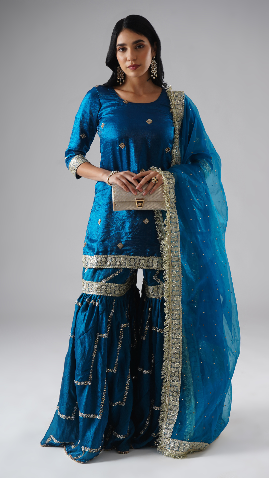 Full outfit of the Neelafshan – The Teal Sapphire gharara set by Zahrat, styled with a clutch, highlighting the gharara, kurta, dupatta, and accessory.