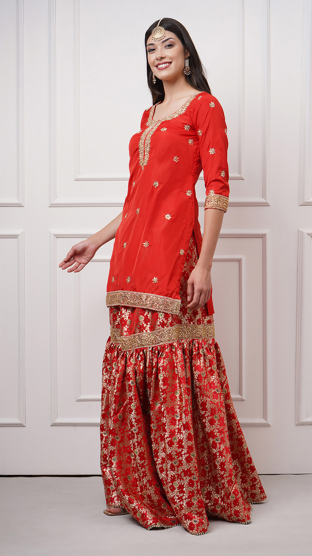 A women models in Surkhnaaz – Red Kimkhwab Bridal Gharara Set by Zahrat showcasing the beautiful kurta and the gharara flare.