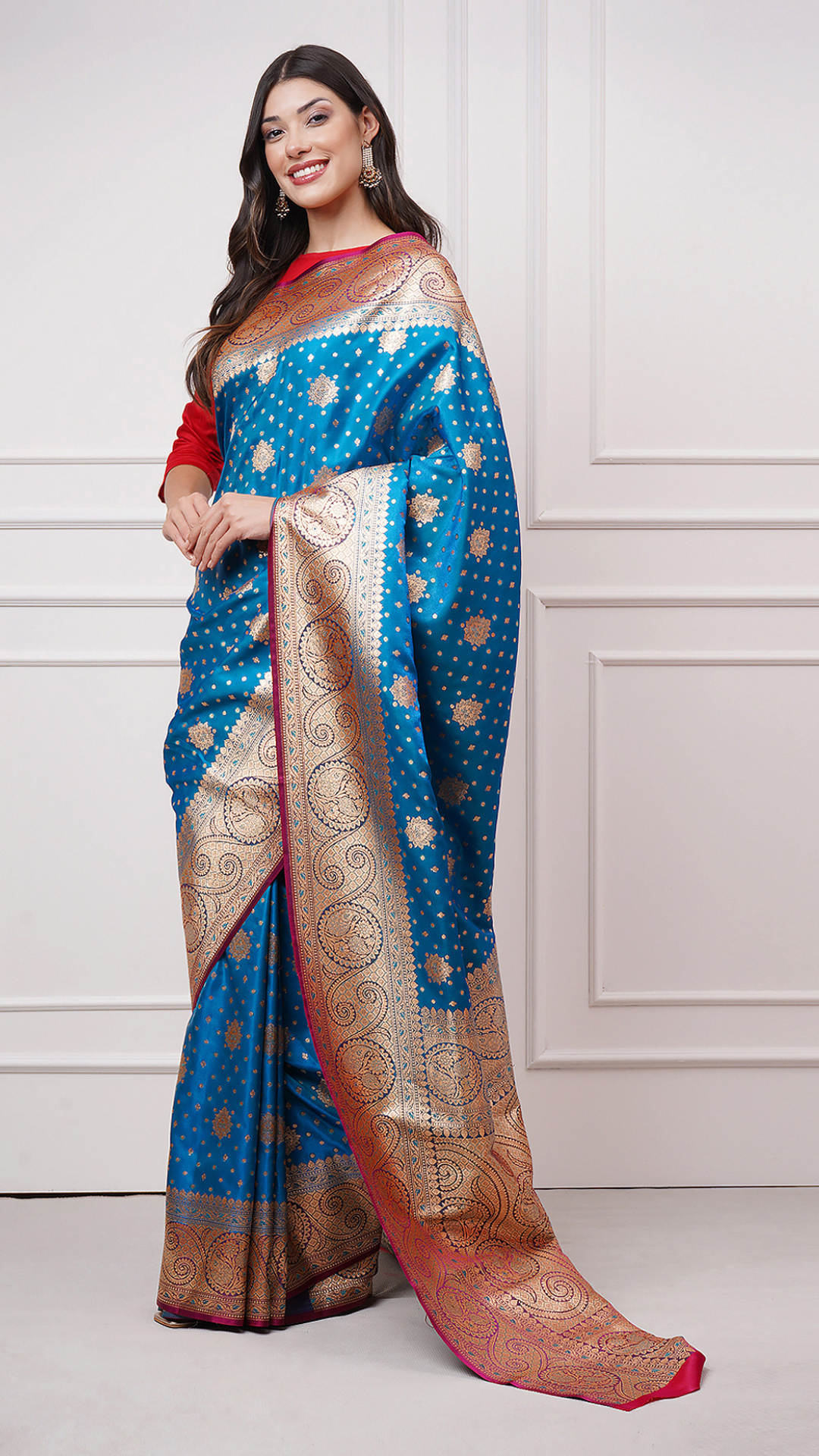A woman models in Taraani – Midnight Sapphire Saree by Zahrat. A blue and gold Banarasi saree. - front left view.