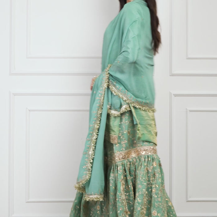 Video of a model wearing the Zahrat Nooraniya – Pastel Jade Gharara Set, walking gracefully and twirling to showcase the fluid flare of the gharara pants. The pastel jade-green fabric shimmers softly under the light, revealing delicate tone-on-tone embroidery on both the kurta and gharara for an elegant, festive look.